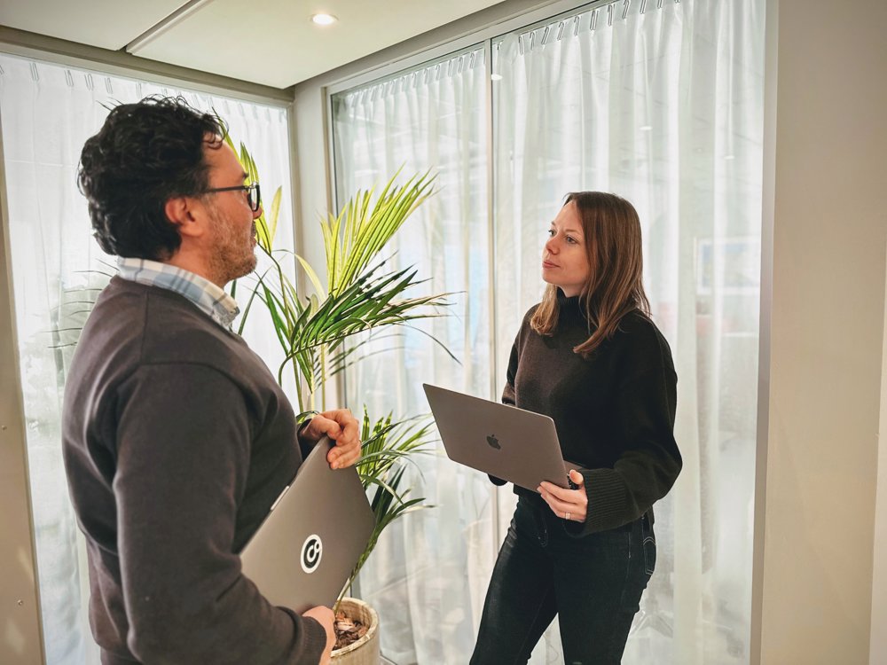 Två personer diskuterar med varsin bärbar dator i hallen.