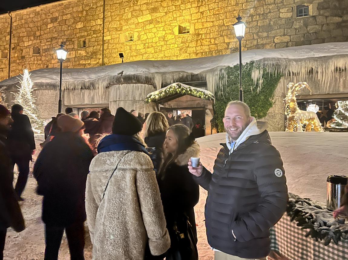 En festlig julträff med snö, dekorationer och glada besökare i bakgrunden.