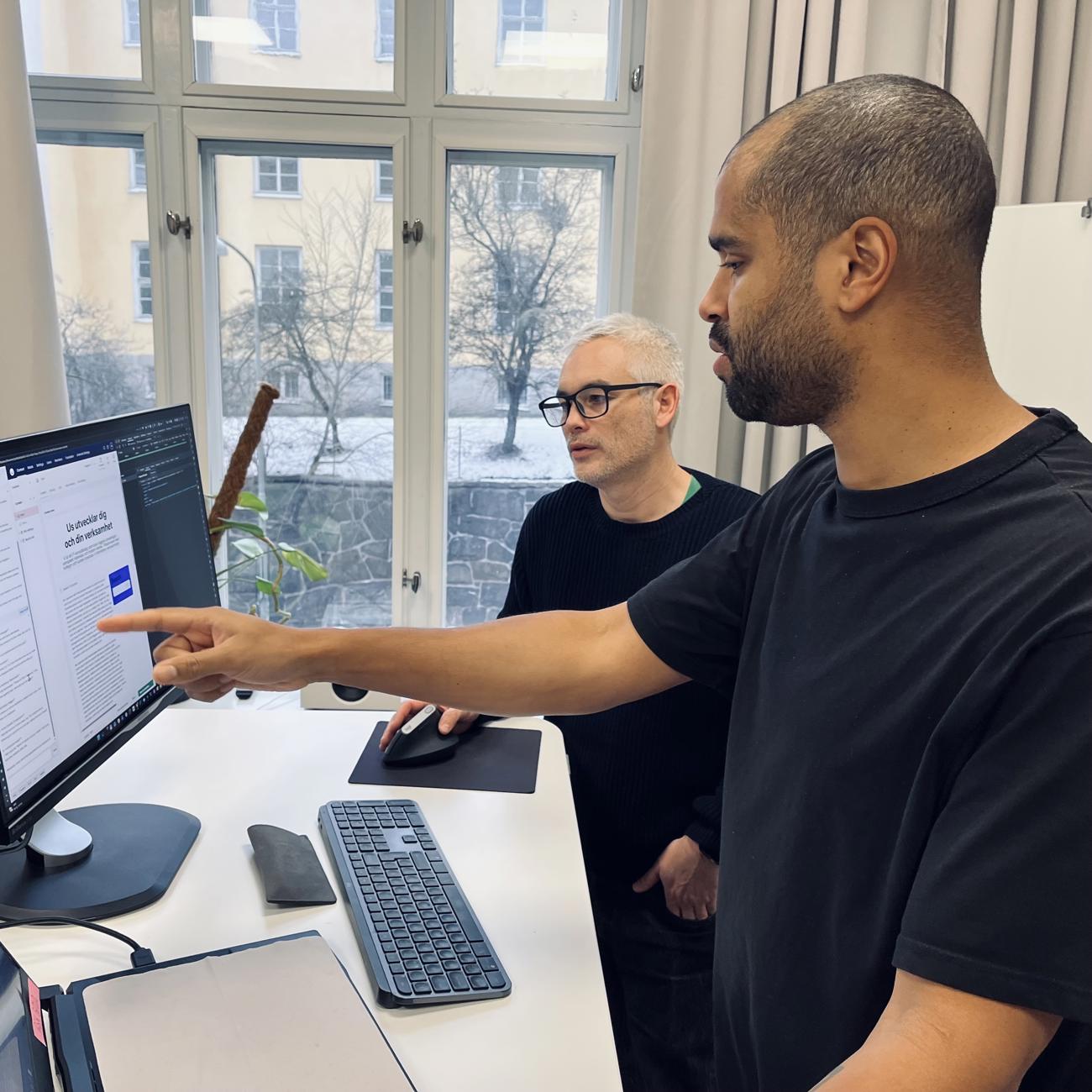 Inomhusmiljö med två män vid en dator, en pekar och den andra ser på skärmen.