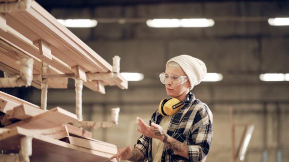 En hantverkare i mössa inspekterar träplankor i en industriell miljö.